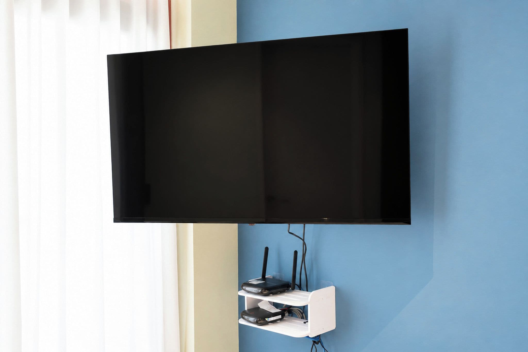 A flat-screen TV mounted on a wall with a cable management box below it.