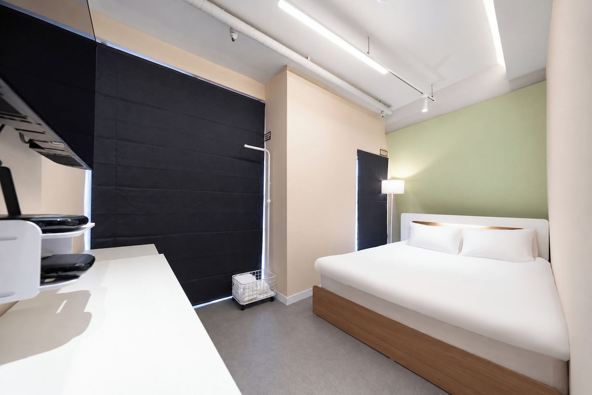 A modern hotel room with a bed, a desk, a chair, and a window.