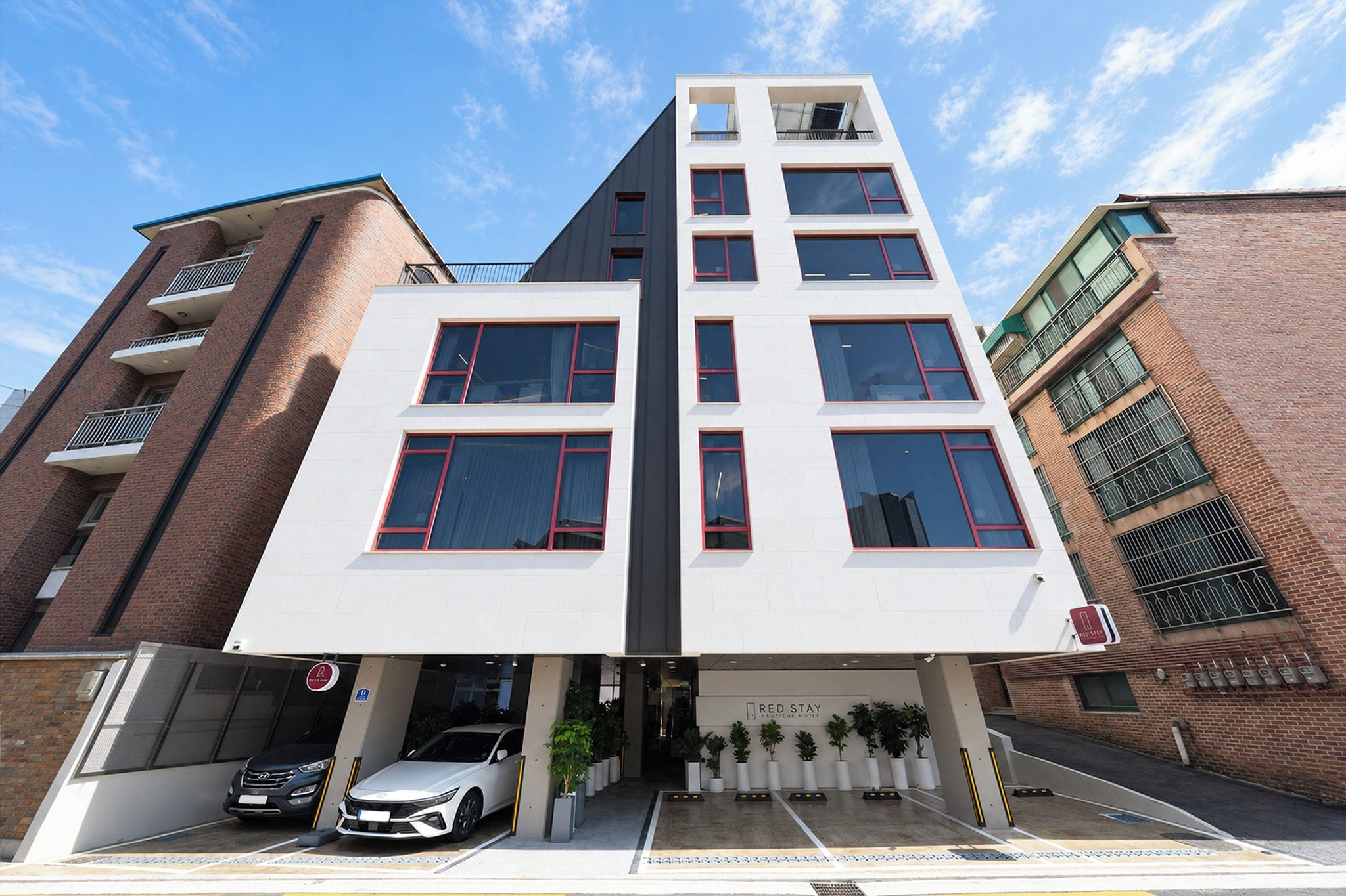 A modern building with a white facade, multiple windows, and a parking area with cars.