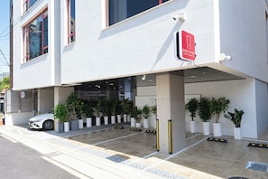 A modern building with a red 'RED STAY' sign, a white car parked outside, and potted plants arranged in rows. - REDSTAY (Seoul)