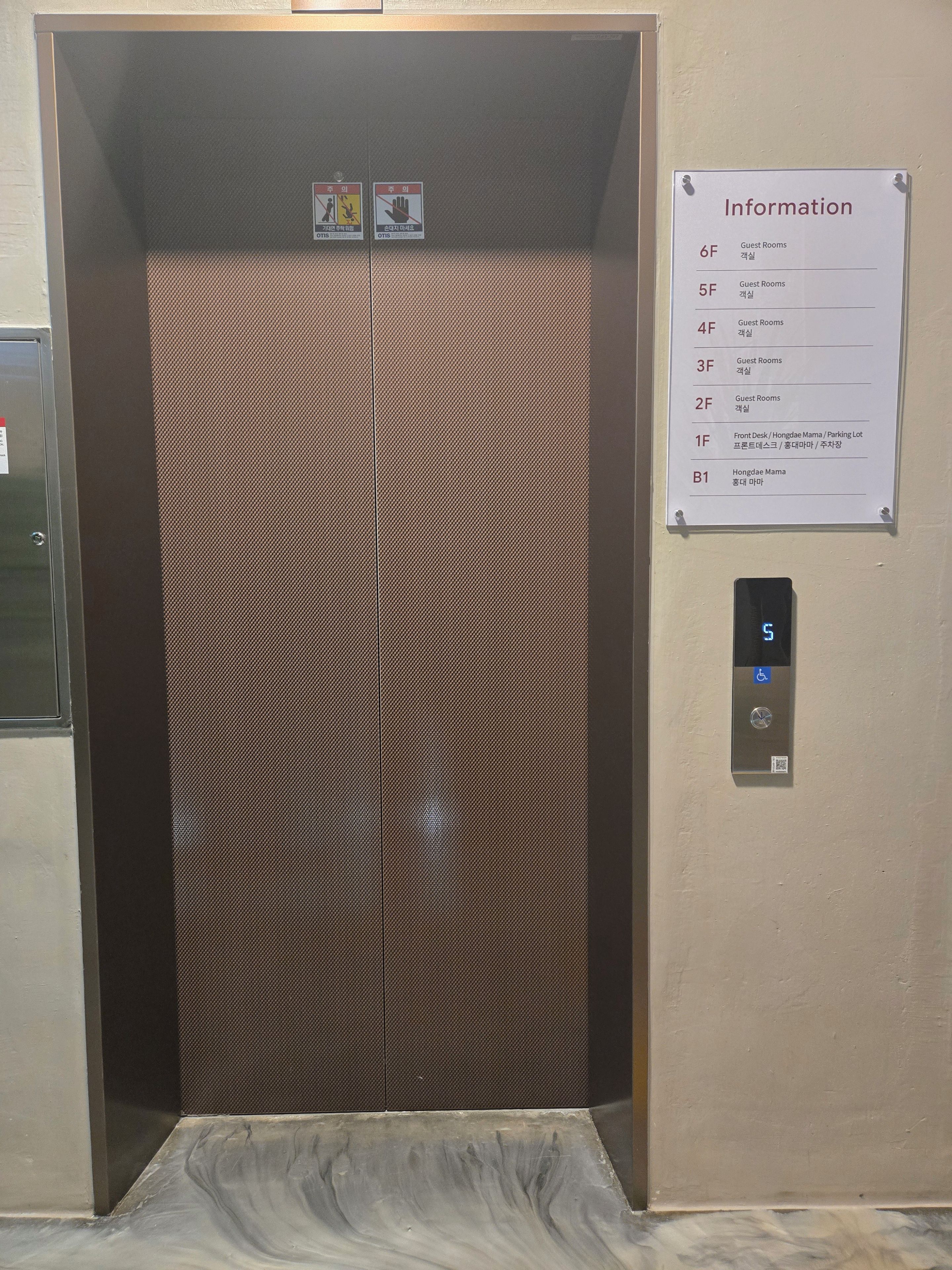 Een lift met een bord waarop de verdiepingen van de gastenkamers staan en een digitaal scherm.