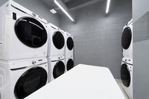 A laundry room with multiple stacked washing machines, a white counter, and grey tiled walls. - REDSTAY (Seoul)