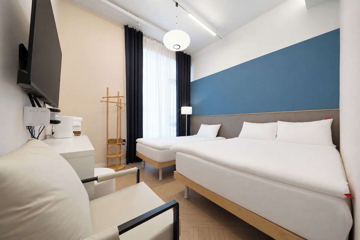 A hotel room with a bed, a desk, a chair, a TV, and a lamp.