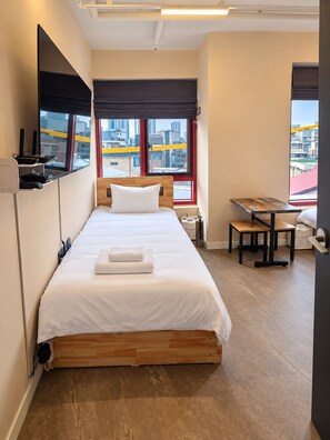 A hotel room with a bed, a desk, and a window with a city view. - REDSTAY (Seoul)