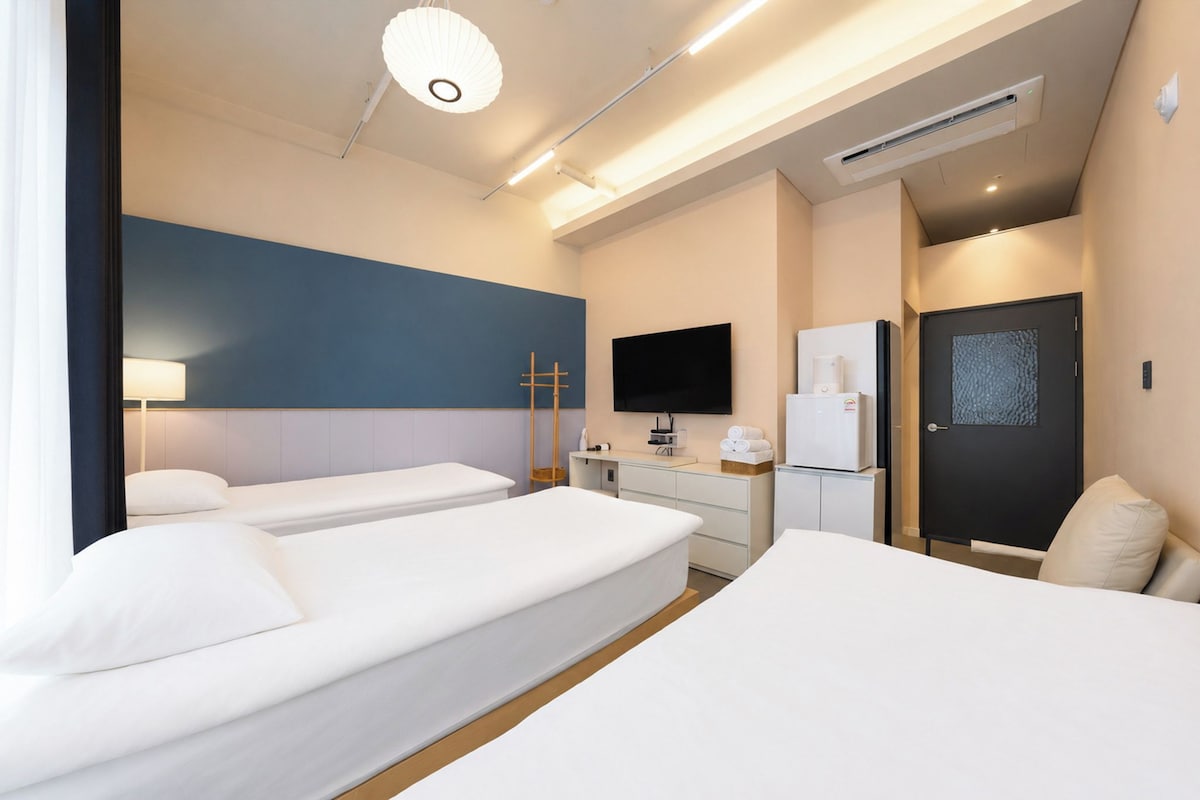 A hotel room with two beds, a flat-screen TV, a minibar, and a door with a textured pattern.