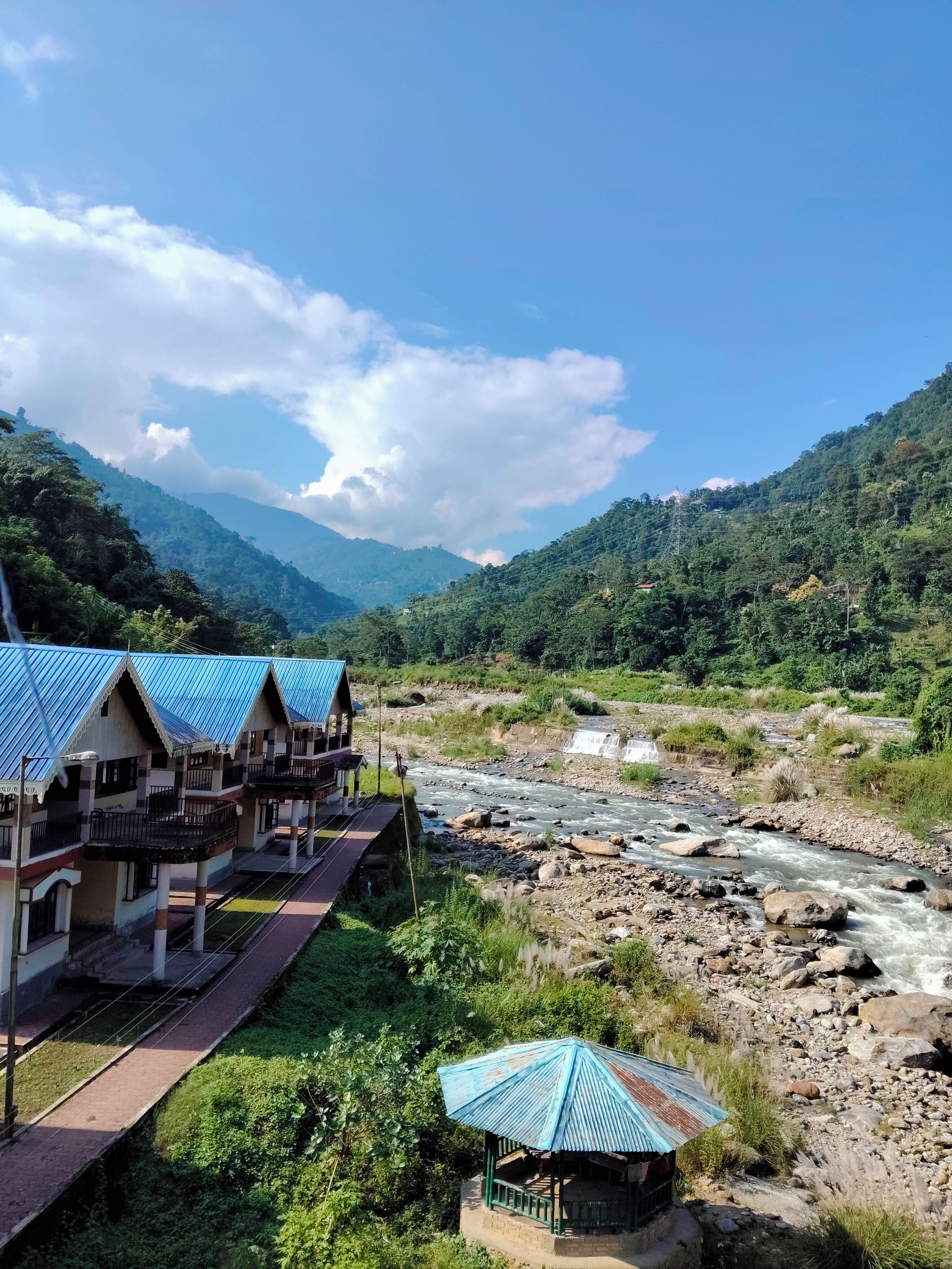A riverside hotel with multiple rooms, a bridge, and a mountainous backdrop.