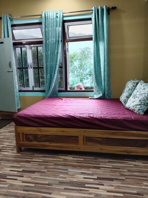 A room with a wooden bed, a window with curtains, and a view of greenery outside.