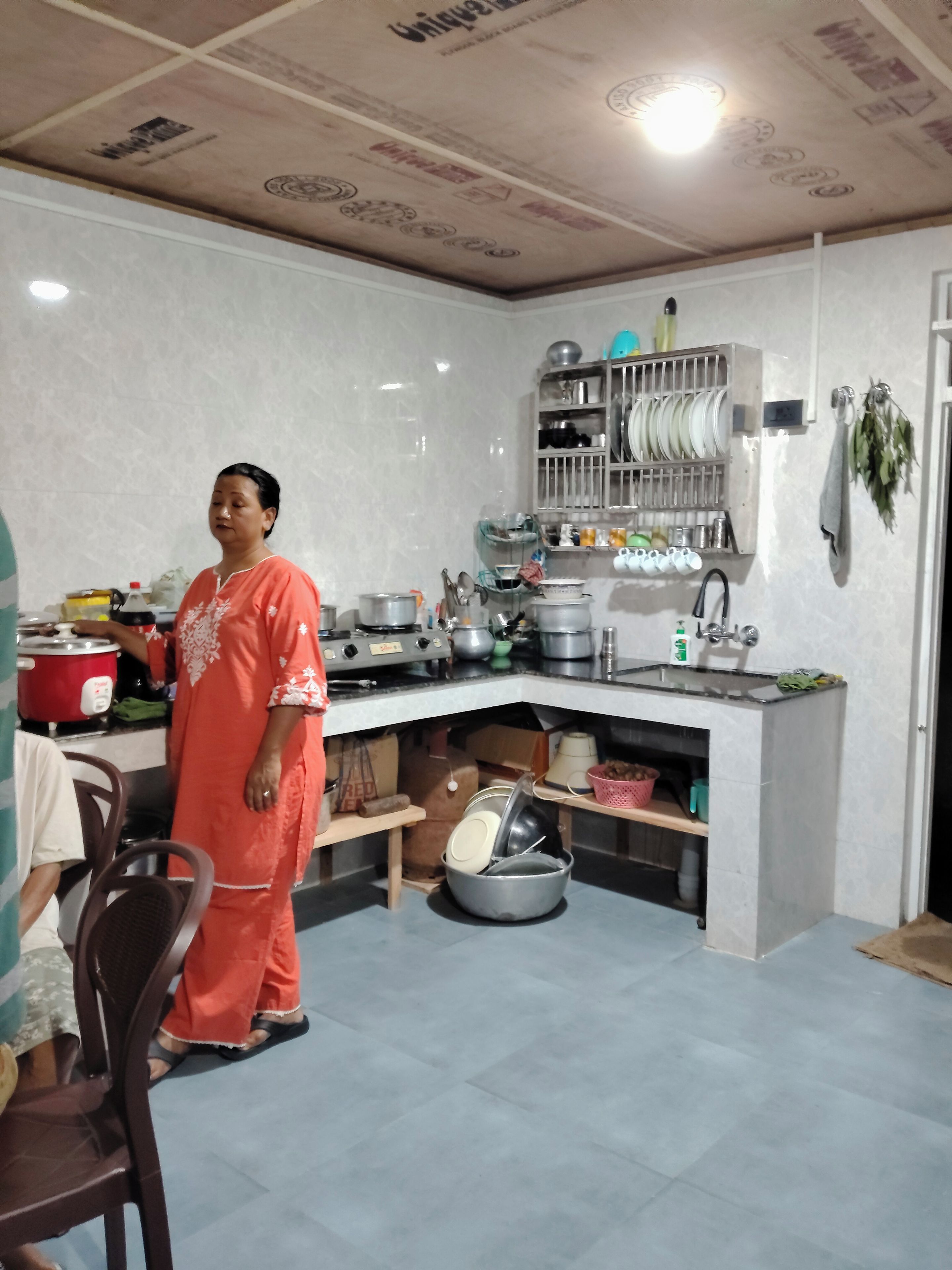 A kitchen with a person standing, a stove, a sink, and various kitchen utensils.