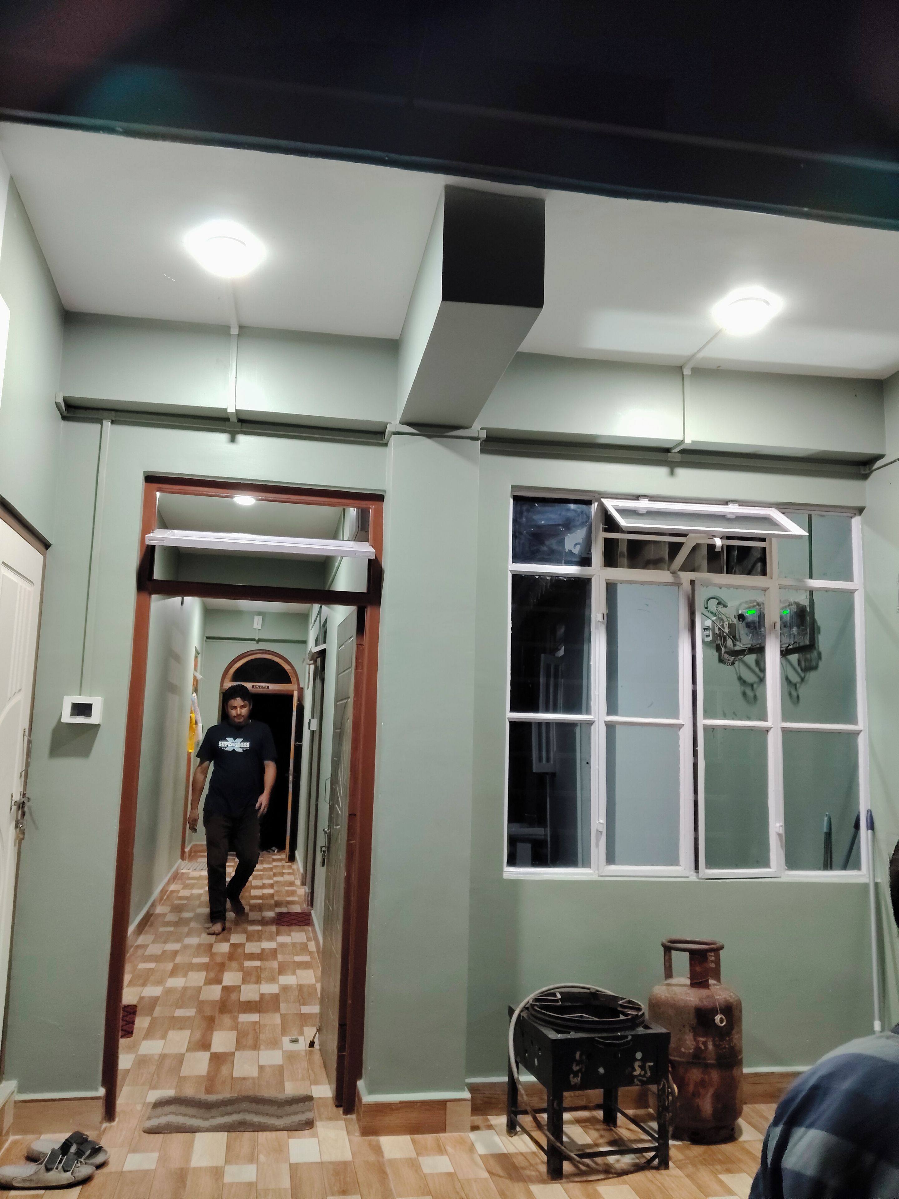 A hallway with a checkered floor, a gas cylinder, and a window with a view of the night sky.