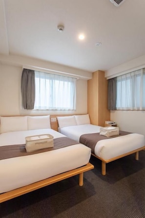 Een hotelkamer met twee bedden, een raam met gordijnen en een plafondlamp.