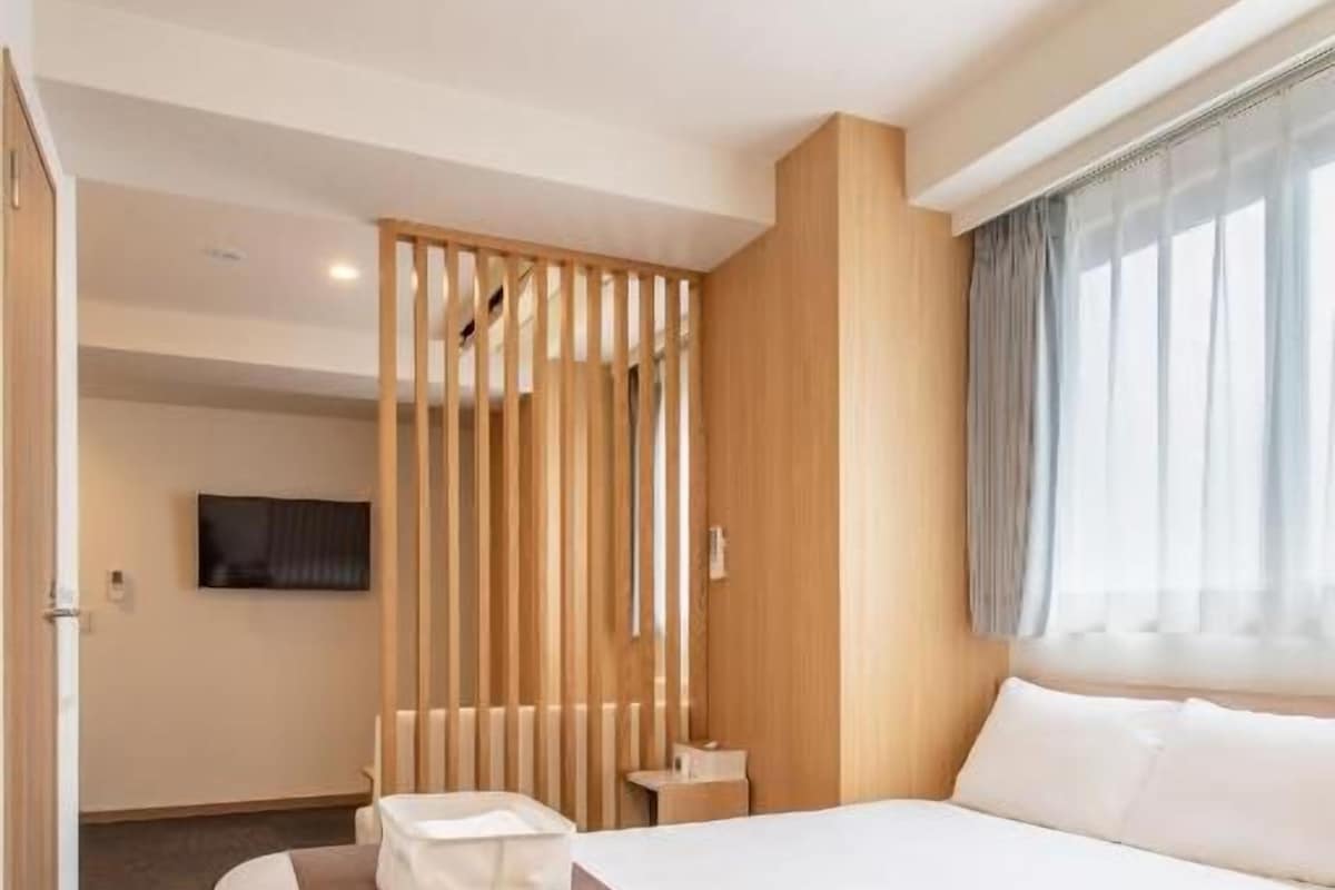 Een hotelkamer met twee bedden, een houten scheidingswand, een televisie en een raam met gordijnen.