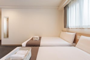 Een hotelkamer met twee bedden, een kleine tafel, een dienblad met handdoeken en een raam met gordijnen.
