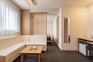 Een hotelkamer met een bank, een eettafeltje, een bureau, een spiegel en een scheidingswand.