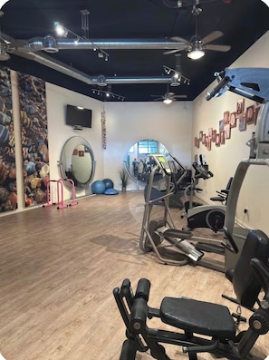 Ein Fitnessraum mit Trainingsgeräten, einem Spiegel und einer Wand mit gerahmten Bildern.