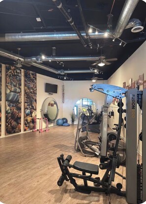 A gym with exercise equipment, a wooden floor, and a wall with a circular mirror. - Casa Sol e Mare Beachfront Getaway by Redondo Pier (Redondo Beach)