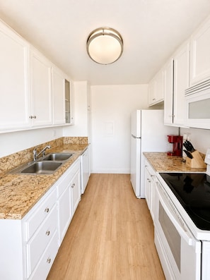 A kitchen with white cabinets, granite countertops, a stainless steel sink, a red coffee maker, and a black stove. - Casa Sol e Mare Beachfront Getaway by Redondo Pier (Redondo Beach)