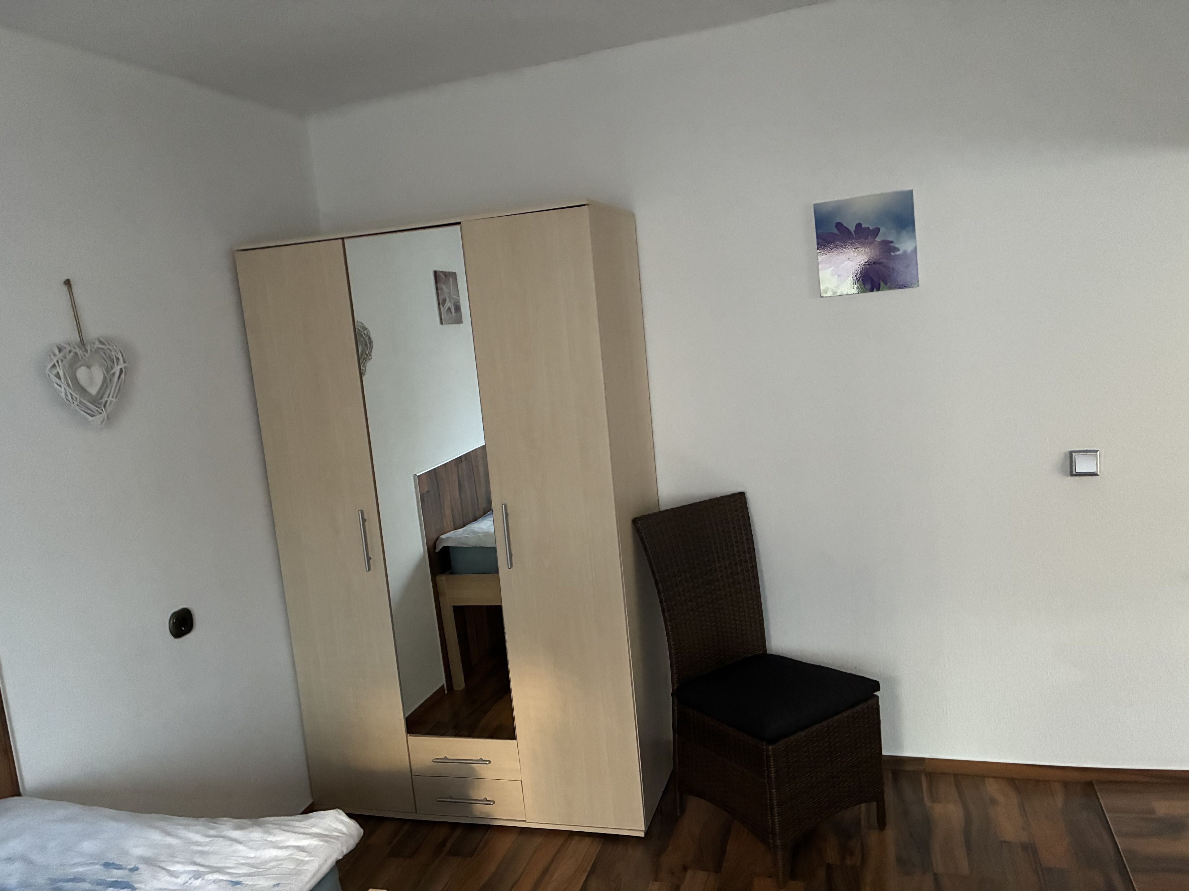 Ein Schlafzimmer mit Kleiderschrank, einem Sessel, einem Bett und einer kleinen Wanddekoration.