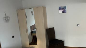 Ein Schlafzimmer mit Kleiderschrank, einem Sessel, einem Bett und einer kleinen Wanddekoration.