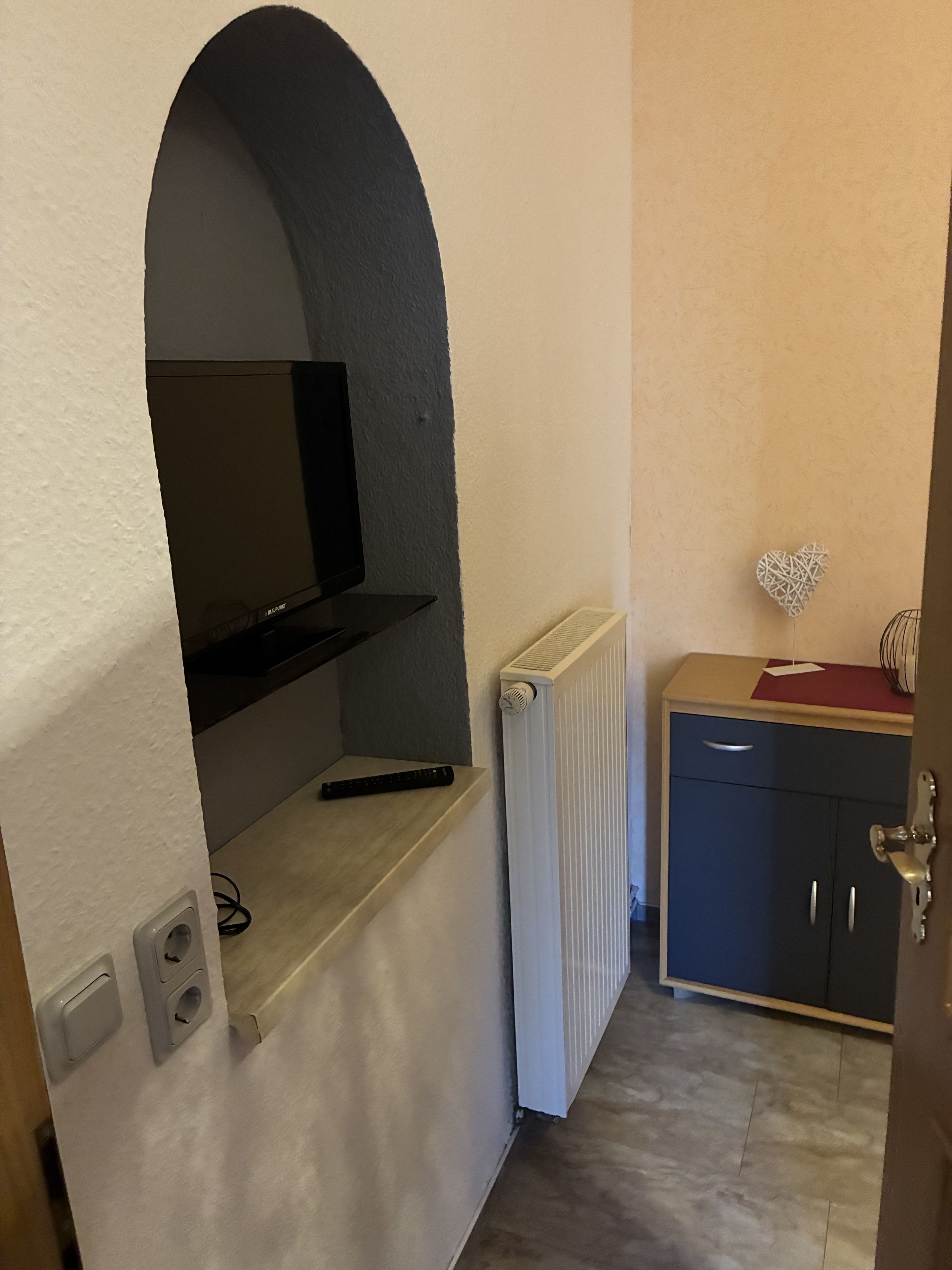 Une cuisine compacte équipée d’un téléviseur encastré, d’un radiateur et d’un petit meuble de rangement.