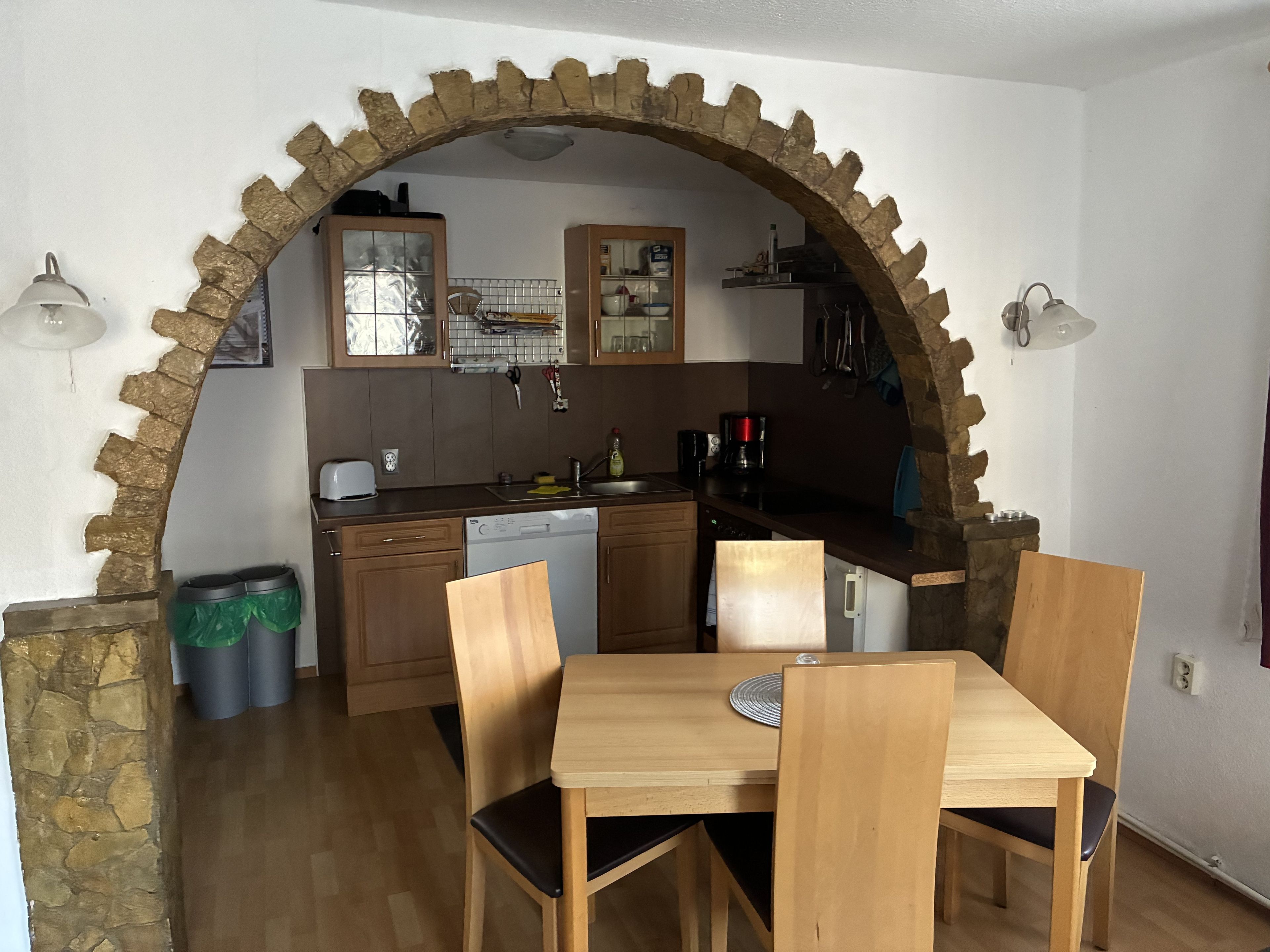 Une cuisine avec une arche en pierre, des meubles en bois, un lave-vaisselle et une table à manger avec des chaises.
