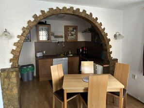 Eine Küche mit steinernen Bögen, Holzschränken, einem Geschirrspüler und einem Esstisch mit Stühlen.