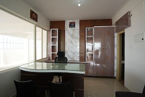 A modern office space with a glass table, two chairs, a cabinet with glass doors, and a wall-mounted shelf. - SHARVI HOTELS (Shrirangapattana)