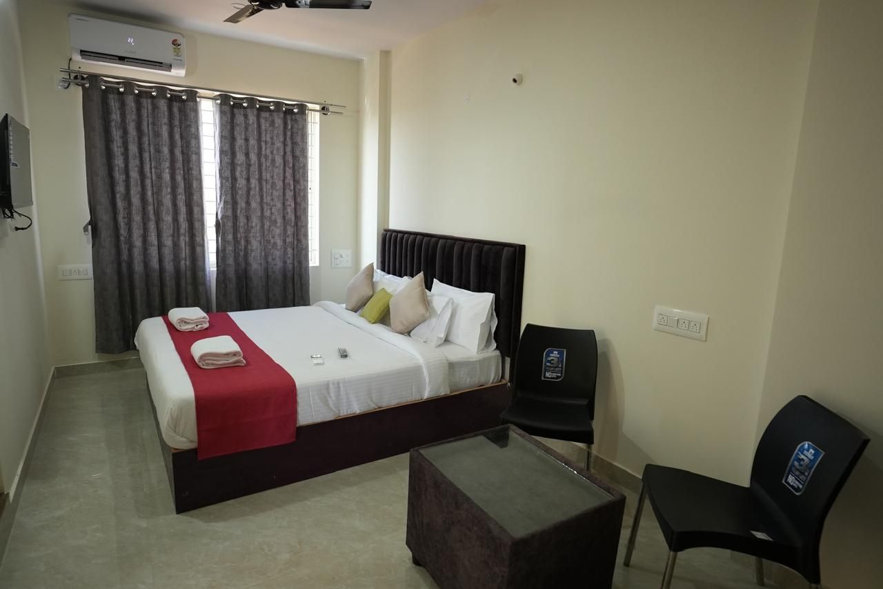 Una habitación de hotel con cama, escritorio, silla, televisor y aire acondicionado.