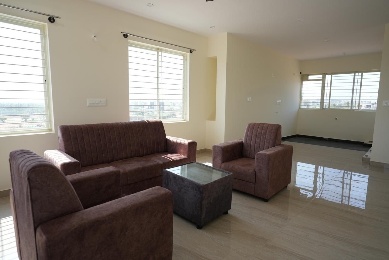 A spacious living room with a sofa set, a coffee table, and large windows.