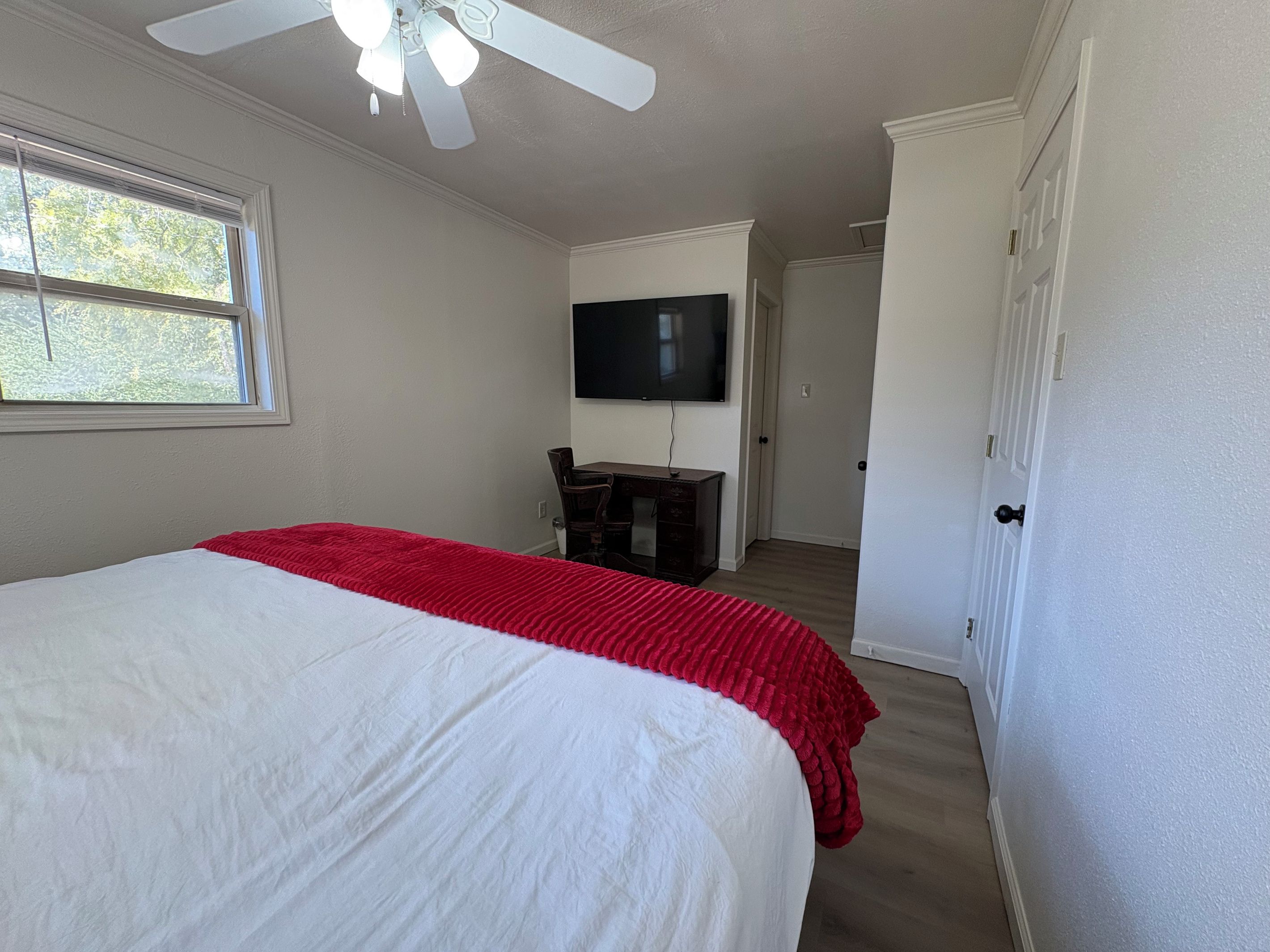 Un dormitorio con una cama, un escritorio, una silla, un televisor y una puerta.