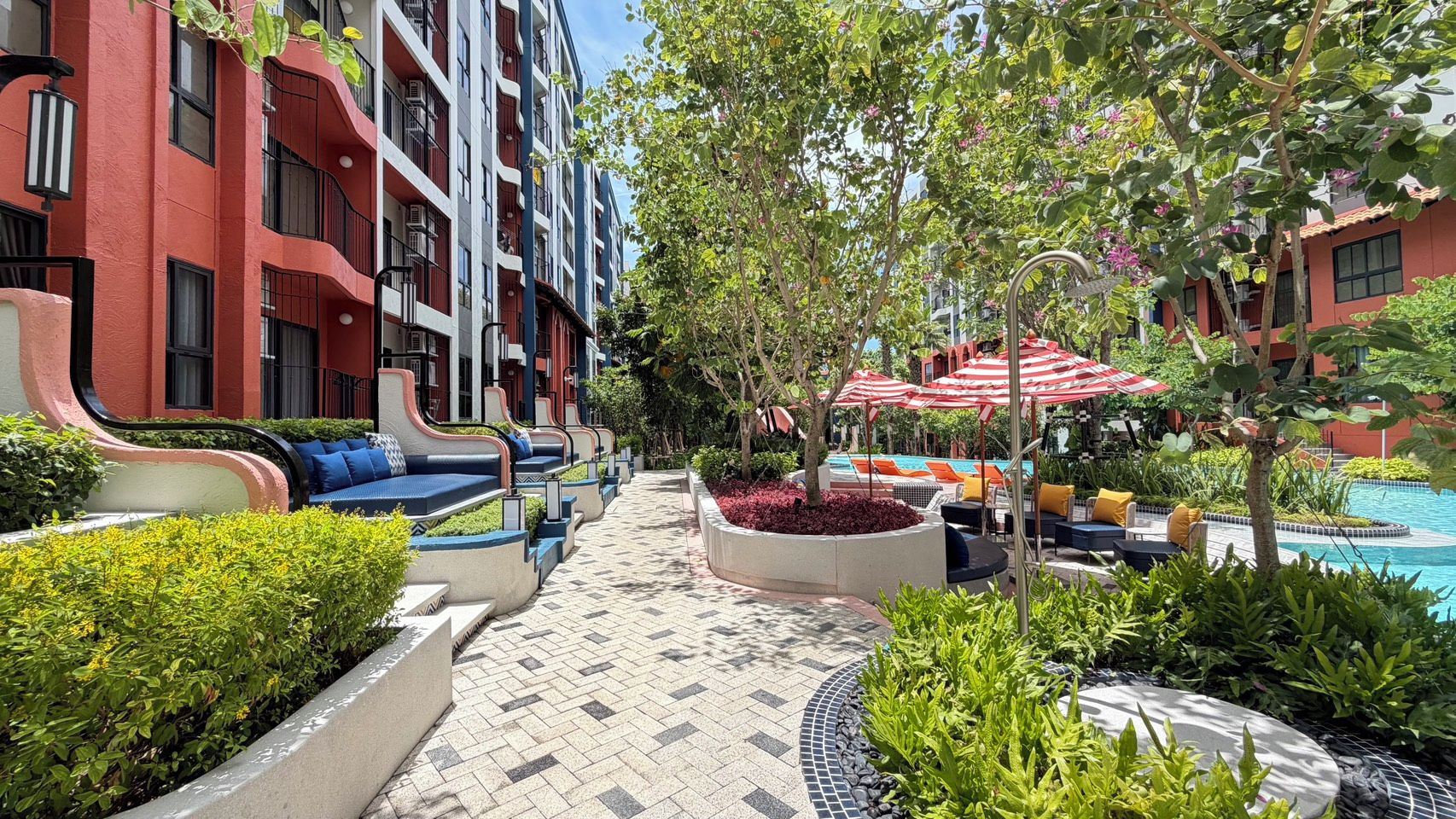 Un patio de hotel con mobiliario exterior, piscina y un edificio rojo con balcones.