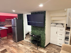 A modern kitchen with a flat-screen TV mounted on a green wall, a refrigerator, and a dining area with a black shelf. - Loft (double-height) on the boardwalk, half a block from the beach (Puerto Vallarta)