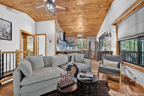 A spacious living room with a wooden ceiling, a grey sectional sofa, a small coffee table, and a dining area in the background. - Woodland Hideaway | Hot Tub, Fire Pit & Fenced Yrd (Blue Ridge)
