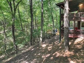A cabin with a deck and a covered porch, surrounded by a forested area. - Woodland Hideaway | Hot Tub, Fire Pit & Fenced Yrd (Blue Ridge)