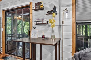 A room with a wooden table, a glass vase with yellow flowers, a framed picture, and a floor lamp. - Woodland Hideaway | Hot Tub, Fire Pit & Fenced Yrd (Blue Ridge)