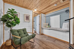 A room with a wooden ceiling, a green chair, a large plant, a framed picture, and a bench with a cushion. - Woodland Hideaway | Hot Tub, Fire Pit & Fenced Yrd (Blue Ridge)