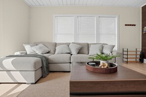 Ein stilvolles Wohnzimmer mit einer Couch, einem Hocker, einem Couchtisch und einer Pflanze.