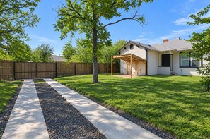 Ein Garten mit überdachter Terrasse, Holzlattenzaun und gepflegtem Rasen.