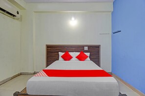 Habitación de hotel con cama, cabecera de madera, colcha roja y blanca, y una pared de acento azul.