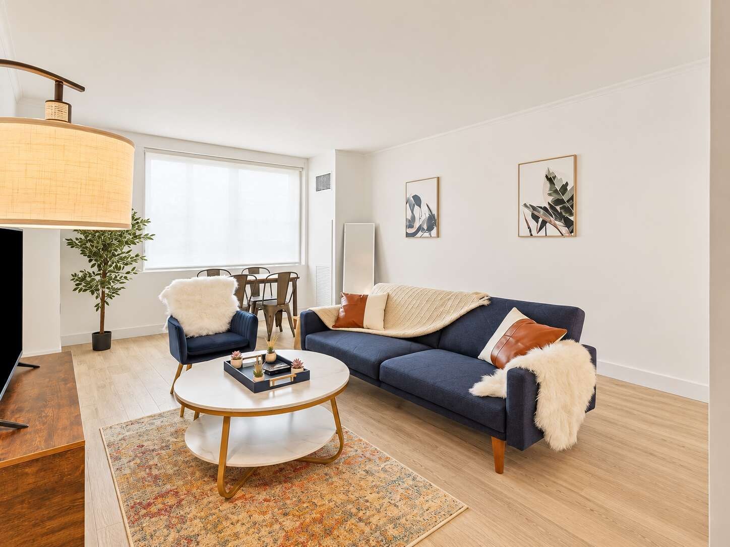 Ein modernes Wohnzimmer mit einem blauen Sofa, einem runden Couchtisch und einem Essbereich mit Stühlen.