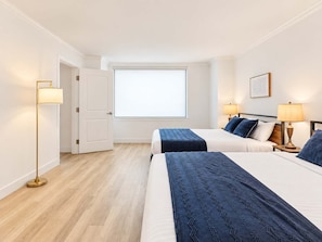 Ein Hotelzimmer mit zwei Betten, einem großen Fenster, einer Stehlampe und einem gerahmten Bild an der Wand.
