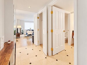 A hallway with a wooden floor, white doors with gold handles, and a dining area in the background. - TWO Separate Bold Ocean Front Condos CozySuites (Atlantic City)