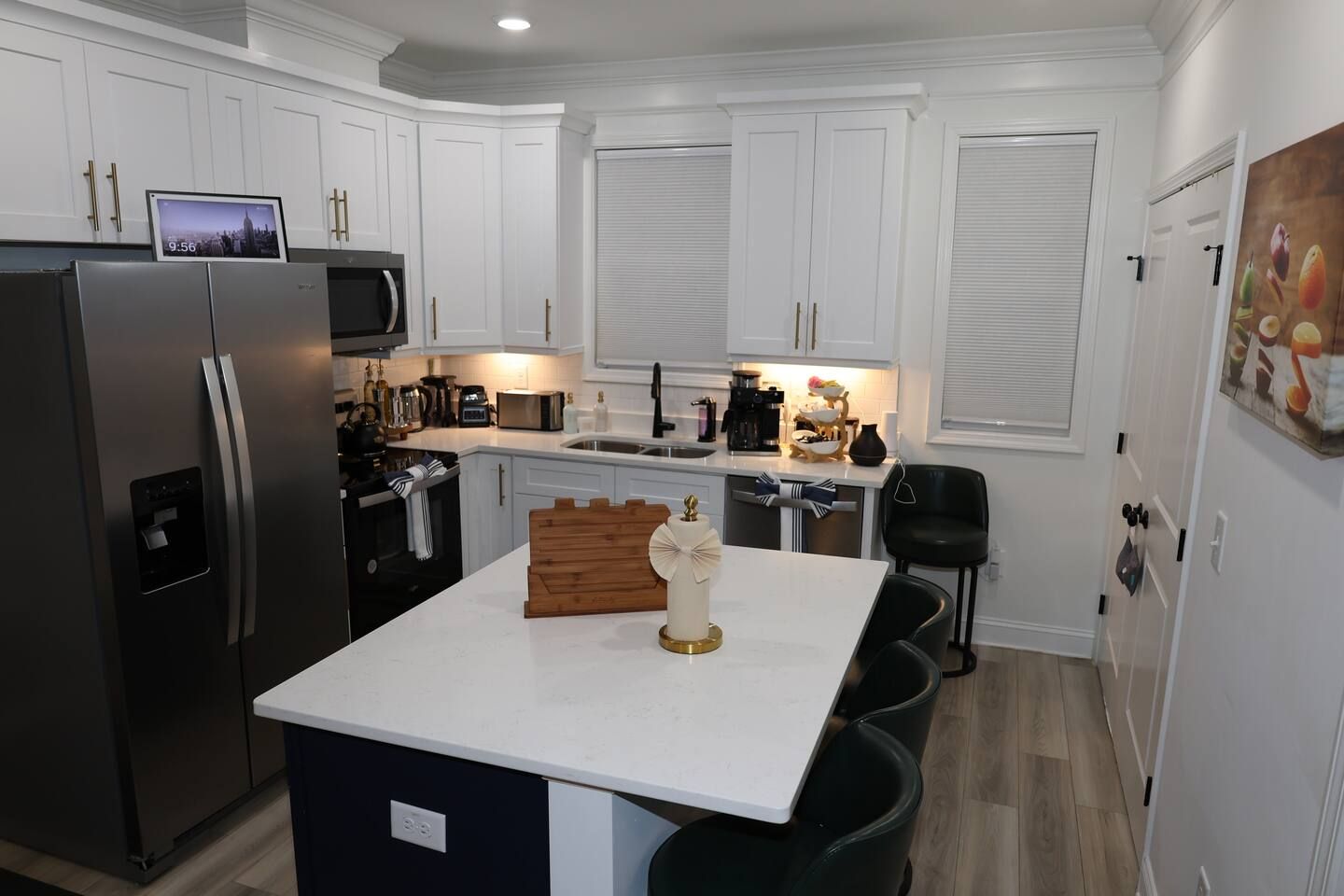 A modern kitchen with white cabinetry, a stainless steel refrigerator, a microwave, and a wooden island with a decorative centerpiece.