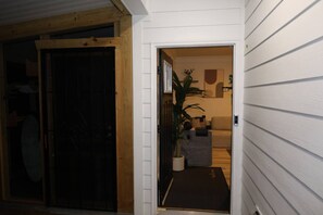 A hallway with a wooden door, a potted plant, and a sofa in a room with white walls. - Elegant, Centrally-Located, Comfy Guest House. (Durham)
