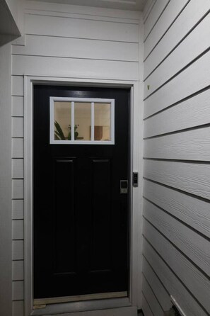 A black door with a small window, white siding on the walls, and a doorbell. - Elegant, Centrally-Located, Comfy Guest House. (Durham)