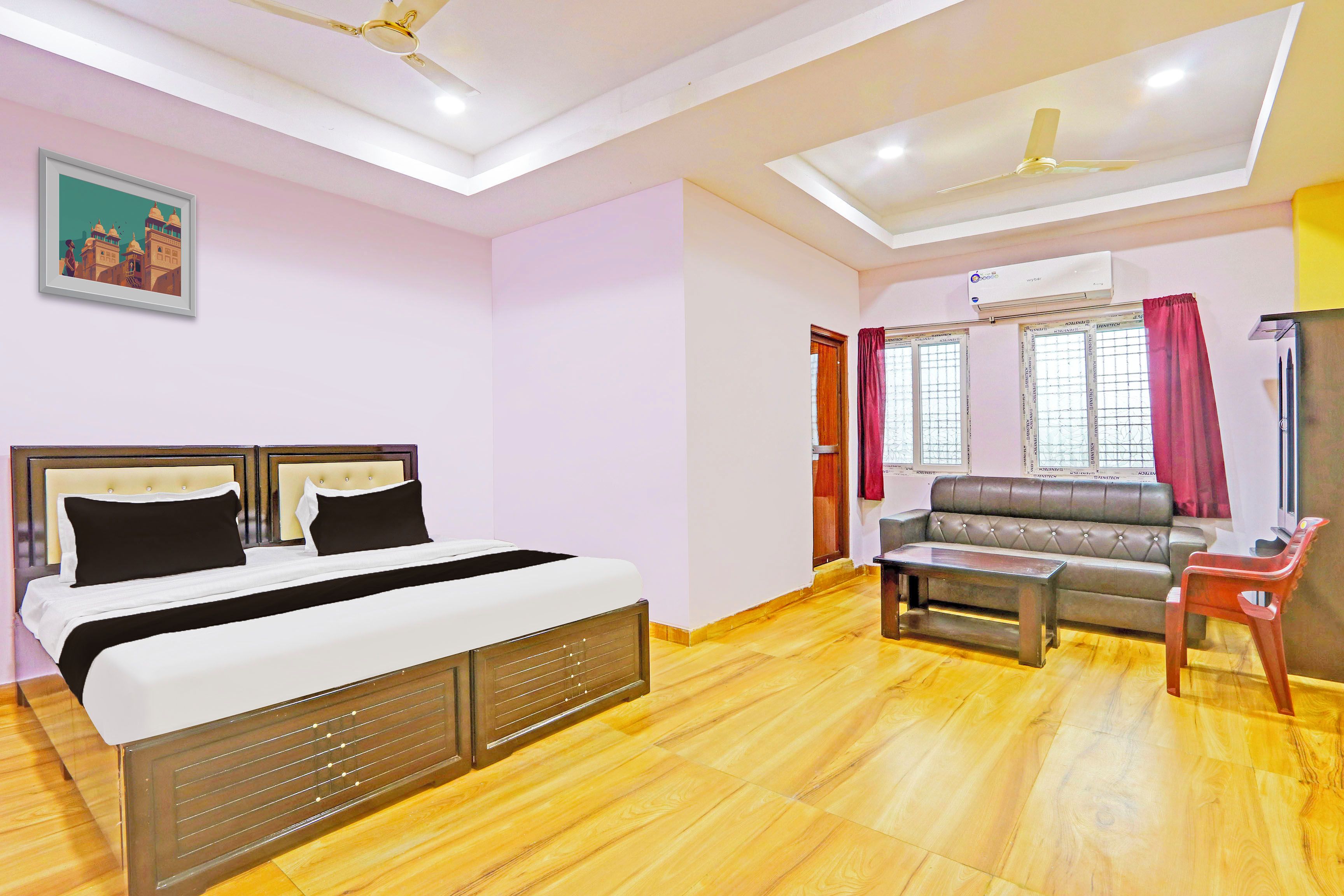 A hotel room with a bed, a sofa, a small table, and a ceiling fan.