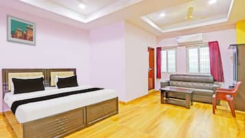 A hotel room with a bed, a sofa, a small table, and a ceiling fan.