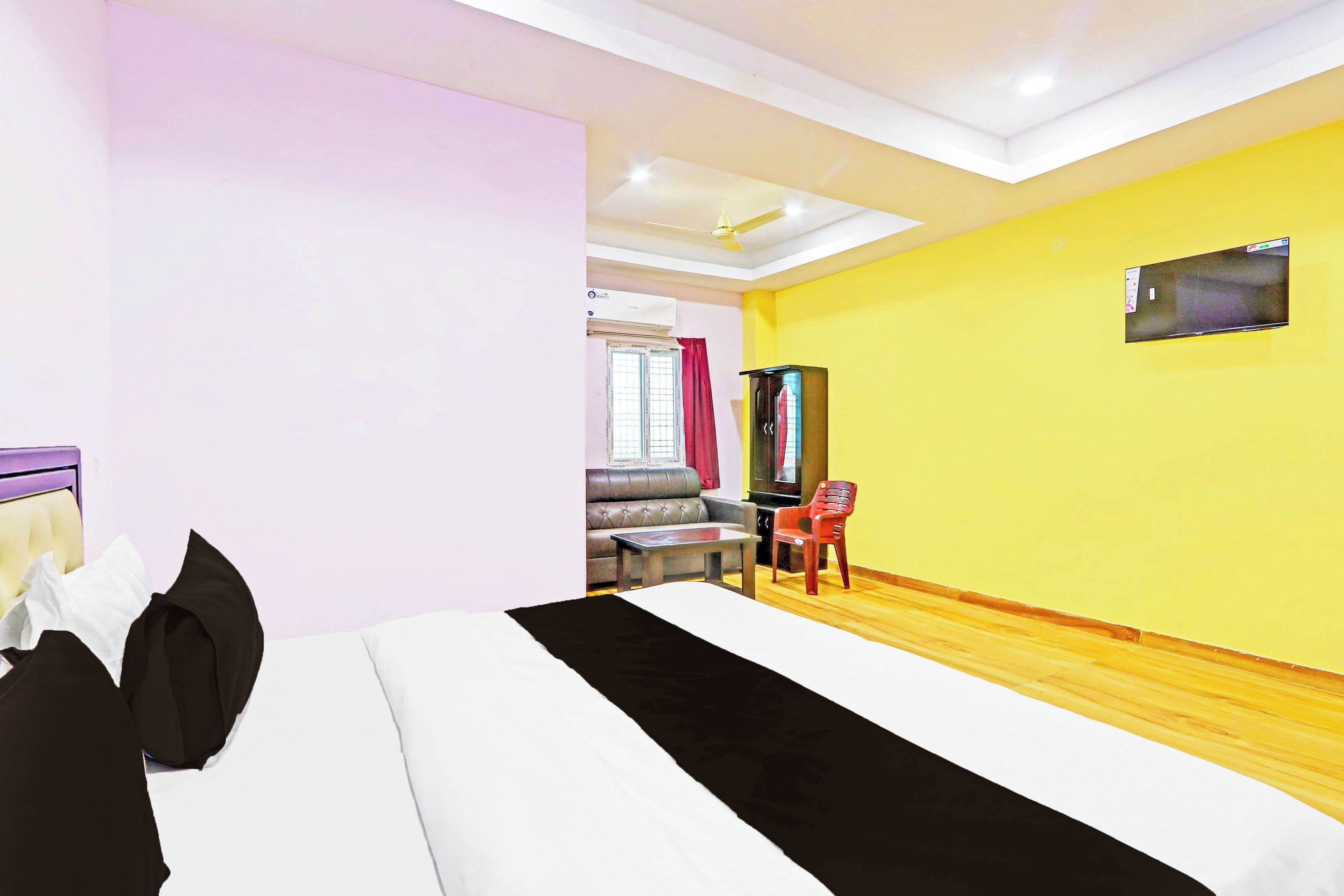 A hotel room with a bed, a desk, a chair, a TV mounted on the wall, and a window with curtains.