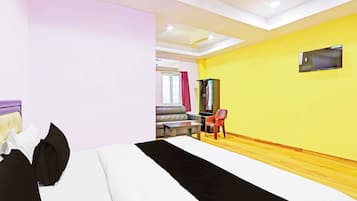A hotel room with a bed, a desk, a chair, a TV mounted on the wall, and a window with curtains.