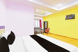 Una camera d'albergo con un letto, una scrivania, una sedia, una TV a parete e una finestra con tende.