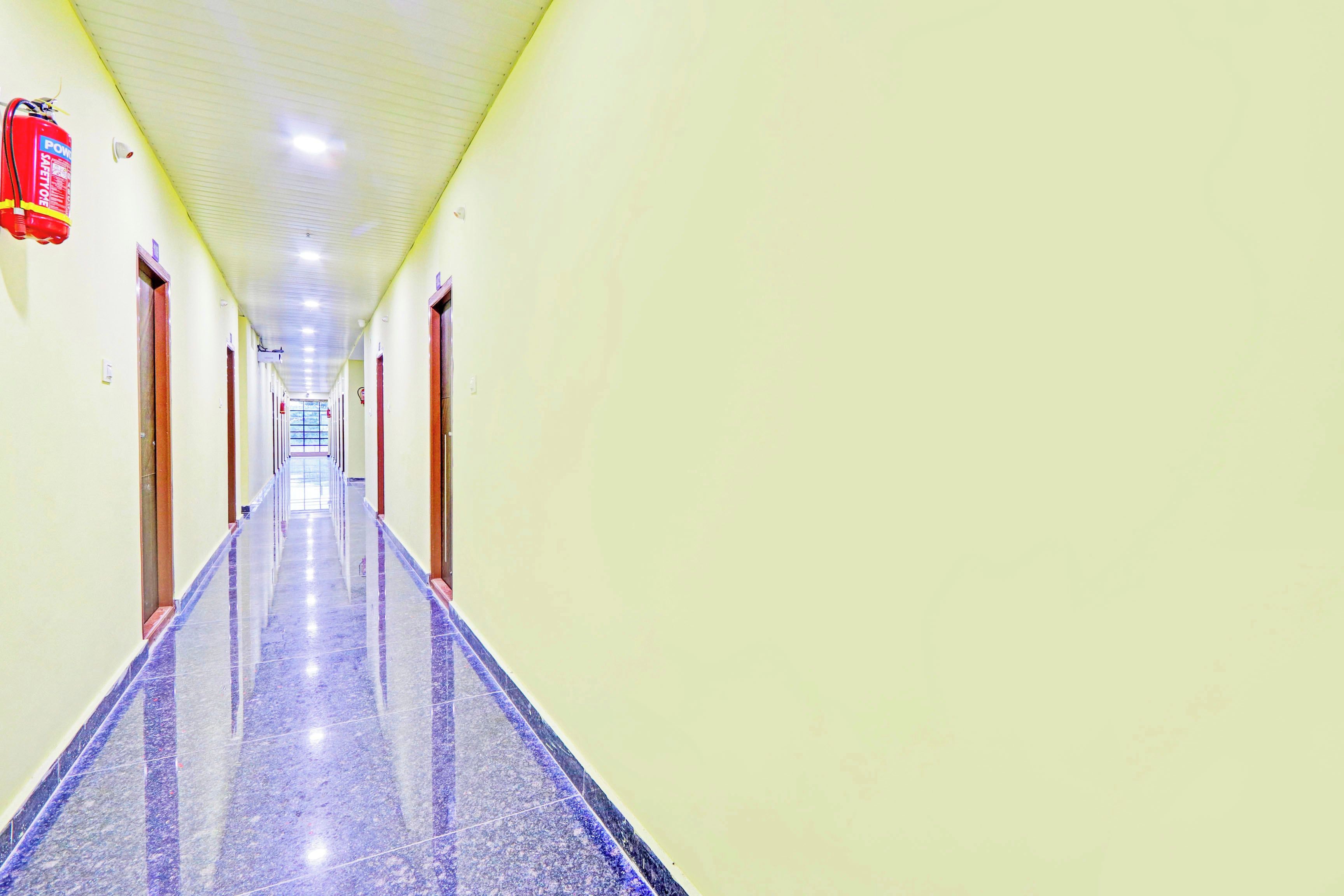 A long, narrow hallway with a fire extinguisher mounted on the wall, a ceiling with recessed lighting, and a door at the end.